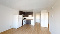 This single-floor unit offers a practical and well-organized layout designed for comfortable everyday living. The open-concept main area seamlessly connects the living space to the kitchen, both finished with warm light-toned laminate flooring throughout. The kitchen is equipped with dark espresso-toned cabinetry — both upper and lower — paired with a neutral laminate countertop, a stainless steel sink, a white electric coil range with overhead ventilation, and ample storage space. A textured popcorn ceiling runs throughout the unit, adding a classic finish.

The bedroom is a well-proportioned room featuring the same laminate flooring, neutral white walls, and a built-in sliding-door closet with multiple shelving levels, providing generous storage. A wall-mounted unit is also visible, offering climate control convenience.

The bathroom is efficiently designed with tile flooring, a dark wood-finish vanity with an integrated sink and large mirror, a toilet, and a tub-shower combination enclosed by sliding frosted glass doors with chrome framing. A ventilation vent is positioned in the ceiling above.

Overall, the unit presents a clean, functional aesthetic with a neutral color palette, making it a versatile and move-in ready space.