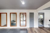 This fitness center offers a thoughtfully designed, single-floor exercise space that provides ample room for a comprehensive workout experience. The open layout is finished with durable hardwood-style flooring throughout, complemented by crisp white walls and a dark gray ceiling with recessed lighting that gives the space a modern, energetic ambiance.

The facility is well-equipped with a diverse range of exercise machines, including treadmills, ellipticals, a cable weight machine, a rowing machine, and a multi-function strength training station, catering to both cardio and resistance training needs. A dedicated stretching and floor exercise area features protective rubber matting, a weight bench, and full-length mirrors framed in warm wood accents, ideal for focused strength or flexibility work.

Natural light filters in through large windows, with views of an outdoor pool area, enhancing the overall workout environment. A wall-mounted television is positioned near the cardio equipment for entertainment during exercise. The space also includes a climate control unit, ensuring comfort year-round. Structural columns punctuate the open floor plan, adding an architectural dimension while maintaining the room's generous, unobstructed feel. A posted rules board and safety equipment round out this practical and inviting fitness facility.