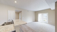 Located at 4100 Lakeview Crossing in Columbus, Ohio, this two-bedroom, one-bathroom residence offers a practical and well-appointed single-floor layout. The open-concept kitchen and living area serves as the heart of the home, where rich dark cabinetry reaches toward the ceiling, providing ample storage. Light granite-style countertops and a breakfast bar complement the black appliances, including a range, over-the-range microwave, and refrigerator. Durable wood-look flooring runs throughout the kitchen and transitions seamlessly into the carpeted living room, which is bright and airy thanks to sliding glass doors that open to a private balcony with outdoor views. The two bedrooms are carpeted and finished in warm neutral tones. The primary bedroom is a comfortable size and includes access to a spacious walk-in closet with wire shelving. The second bedroom features a window that brings in natural light. The full bathroom is clean and functional, offering a tub/shower combination with white surround, tile flooring, and a vanity with matching dark cabinetry. A hallway connects all rooms efficiently, completing this well-organized and move-in-ready home.