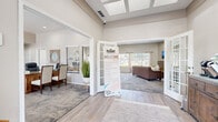 The Patriot Apartments leasing office and clubhouse is a thoughtfully designed single-story facility that serves as the community's central hub. The grand entry welcomes visitors with soaring ceilings accented by coffered details and skylights, wood-look flooring, and an open, airy atmosphere that immediately sets a polished and professional tone.

From the entry, elegant French doors lead into a spacious lounge area furnished with a plush sectional sofa, a wall-mounted flat-screen TV, and a stone-accented fireplace that adds warmth and character. Large windows line the lounge, inviting an abundance of natural light and providing pleasant outdoor views. A dedicated refreshment nook with a coffee station and decorative sideboard offers a comfortable space for residents and guests.

The leasing office area features multiple workstations set on patterned carpet, accompanied by framed artwork and open shelving with tasteful décor. Each desk area is positioned to allow for private consultations in a welcoming, well-lit environment with views to the outside.

A glazed interior window offers a sightline into the fitness center beyond, showcasing exercise equipment and reinforcing the community's commitment to resident amenities. Throughout, the design balances neutral tones, warm wood furnishings, and modern finishes to create a cohesive and inviting environment.