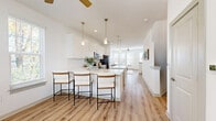 Located at 6026 Station Crossing Ave in Charlotte, NC, this four-story townhome delivers a well-organized layout across multiple levels, offering 3 bedrooms, 5 bathrooms, and a 2-car garage. The entry-level garage is spacious and equipped with an automatic opener, with interior access via a private door. Carpeted staircases with clean railings connect each floor, with light wood-look flooring flowing throughout the main living areas. The main living level features an open-plan kitchen and living room flooded with natural light from large windows dressed in white blinds. The kitchen stands out with white shaker cabinetry extending to the ceiling, a large center island with seating, quartz countertops, stainless steel appliances, and elegant pendant lighting. Ceiling fans are present in both the kitchen and living areas for added comfort. The living room is bright and airy, with multiple windows offering outdoor views. Bedrooms are carpeted and well-lit, with ceiling fans and ample natural light. The primary bedroom features multiple windows. The five bathrooms are finished in a clean, modern style, offering both walk-in glass showers and tub-shower combinations, white vanities, and wood-look flooring — providing convenience and comfort throughout every floor.