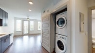 This single-floor residence showcases a contemporary design with a cohesive open layout connecting the kitchen and living areas. The kitchen is well-appointed with dark espresso-toned cabinetry extending to the ceiling, offering generous storage, complemented by light quartz countertops, a textured tile backsplash, and a full suite of stainless steel appliances including a range, microwave, dishwasher, and refrigerator. Wood-tone flooring runs throughout the space, adding warmth and visual continuity.

The living area receives abundant natural light through multiple large windows fitted with horizontal blinds, framing views of the outdoors. A ceiling fan is centrally positioned, providing both airflow and subtle ambient light. A dedicated in-unit laundry closet houses a stacked washer and dryer, adding practical convenience.

The bedroom is comfortably sized with a ceiling fan, a window for natural light, and access to a walk-in closet with rod and shelf storage. The bathroom features a deep soaking tub with a shower, fully enclosed by classic white subway tile, paired with brushed nickel fixtures for a clean, timeless finish. Overall, the space presents a modern, functional aesthetic throughout.