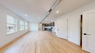 This thoughtfully designed single-floor unit offers a generous open-concept layout finished with light natural hardwood flooring throughout, creating a cohesive and airy aesthetic across all rooms. The living area is bright and spacious, benefiting from large windows that invite abundant natural light, with an exposed metallic ductwork detail adding an industrial accent to the clean white ceilings fitted with recessed lighting.

The kitchen is a standout feature, outfitted with a full suite of stainless steel appliances including a gas range, built-in microwave, dishwasher, and refrigerator. Dark wood-grain cabinetry with matte black hardware is paired with crisp white countertops and a deep undermount sink with a matte black faucet, delivering a sharp, contemporary look.

The individual rooms are well-proportioned with clean white walls and recessed lighting throughout. Several rooms feature large windows with views to the outdoors, offering plentiful natural light. A dedicated walk-in closet provides built-in shelving and hanging space for ample storage.

The bathroom is elegantly appointed with marble-patterned tile surrounding the tub and shower enclosure, complemented by a glass sliding door with matte black fixtures, grey floor tile, and open wall shelving — completing this modern, move-in-ready space.