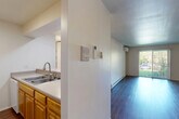 This efficient and thoughtfully designed one-bedroom, one-bathroom unit offers a functional single-floor layout that maximizes every square foot. The living room serves as the central gathering space, featuring rich dark hardwood flooring, a wall-mounted mini-split air conditioning unit, baseboard heating, and a sliding glass door that opens to a view of lush greenery, allowing natural light to fill the room.

The kitchen is positioned adjacent to the living area and is defined by a peninsula counter with a double-basin sink, warm honey-toned wood cabinetry extending to the ceiling, ample counter space, and a full suite of appliances including a refrigerator and range. The pass-through design keeps the kitchen connected to the main living space.

A hallway connects the living area to the private bedroom, which is finished with neutral carpet, a window overlooking mature trees, and baseboard heating. Two closets provide practical storage solutions throughout the unit.

The bathroom is clean and functional, featuring light wood cabinetry with a single-sink vanity, a large mirror, a tub/shower combination, and light-toned flooring. Neutral white walls throughout the unit create a bright, cohesive aesthetic that offers a versatile backdrop for personalization.