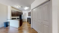 This thoughtfully designed one-bedroom, one-bathroom residence offers a practical and comfortable single-floor layout. The combined kitchen and living area serves as the heart of the home, featuring warm hardwood-style flooring, vaulted ceilings with a ceiling fan, and a sliding door that invites natural light and outdoor access. The kitchen is well-equipped with dark espresso cabinetry, dark granite countertops, white subway tile backsplash, and a full suite of stainless steel appliances including a refrigerator, gas range with microwave, and a double-basin sink set into a peninsula that overlooks the living area. A dedicated hallway leads to the bedroom, which is carpeted for comfort and includes a ceiling fan, a window with blinds, and direct access to both a walk-in closet with built-in shelving and the full bathroom. The bathroom features dark wood cabinetry, a light countertop vanity, wood-style flooring, and a glass-enclosed walk-in shower. Additional storage is provided by a large double-door closet located near the entryway. The entryway hallway features rich hardwood-style flooring and provides a welcoming transition into the main living spaces.
