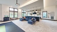 Located at 5151 Patriarch Pl in North Augusta, SC, this impressively scaled single-floor amenity center offers a thoughtfully designed layout across two distinct living areas. The grand entrance lobby sets the tone with soaring vaulted ceilings, herringbone hardwood flooring, floor-to-ceiling black-framed windows, and a dramatic stone accent wall framed by lush greenery. Exposed timber trusses and stacked stone columns add architectural warmth throughout.

The first living area serves as a bright, open lounge with large windows offering outdoor views, herringbone wood floors, and clustered seating around bistro tables — ideal for casual gatherings. A striking geometric tile accent wall with floating shelves and dark cabinetry provides a stylish focal point nearby.

The second living area functions as a media and entertainment lounge, anchored by a large sectional sofa, a ceiling-mounted projector, and a sleek wet bar featuring a fluted island, white quartz countertops, open wood shelving, and bold globe pendant lighting.

A dedicated game room includes a billiard table, foosball, air hockey, a wall-mounted fireplace, and direct access to an outdoor balcony. A state-of-the-art Full Swing golf simulator room rounds out the entertainment offerings, complete with carpeted turf flooring and an exterior-facing window wall.
