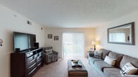 Located on Williamsburg Drive in Augusta, Georgia, this single-floor residence offers a well-organized layout that balances comfort and functionality throughout. The spacious living room is a welcoming centerpiece, featuring plush carpet, a textured ceiling, and a large sliding glass door with vertical blinds that fills the room with natural light and provides access to an outdoor area. The galley-style kitchen is efficiently designed with warm wood cabinetry, granite-look countertops, tile flooring, and black appliances including a refrigerator and range, with a pass-through counter connecting to the adjacent dining area. The dining space comfortably accommodates a full dining set and benefits from its open connection to both the kitchen and living areas. Two carpeted bedrooms offer quiet retreats, each with windows that bring in natural light. The full bathroom features tile flooring, a rich wood vanity with granite countertops, and a shower. A dedicated in-unit laundry area with side-by-side washer and dryer hookups adds significant everyday convenience. Throughout the home, neutral tones and consistent finishes create a cohesive and easy-to-personalize living environment.