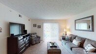 Located on Williamsburg Drive in Augusta, Georgia, this single-floor residence offers a well-organized layout that balances comfort and functionality throughout. The spacious living room is a welcoming centerpiece, featuring plush carpet, a textured ceiling, and a large sliding glass door with vertical blinds that fills the room with natural light and provides access to an outdoor area. The galley-style kitchen is efficiently designed with warm wood cabinetry, granite-look countertops, tile flooring, and black appliances including a refrigerator and range, with a pass-through counter connecting to the adjacent dining area. The dining space comfortably accommodates a full dining set and benefits from its open connection to both the kitchen and living areas. Two carpeted bedrooms offer quiet retreats, each with windows that bring in natural light. The full bathroom features tile flooring, a rich wood vanity with granite countertops, and a shower. A dedicated in-unit laundry area with side-by-side washer and dryer hookups adds significant everyday convenience. Throughout the home, neutral tones and consistent finishes create a cohesive and easy-to-personalize living environment.