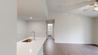 This single-floor unit is designed with a clean, modern aesthetic characterized by white walls, wood-look flooring throughout the main living areas, and an abundance of natural light. The open-concept layout connects the kitchen and living area seamlessly, creating a functional and airy feel.

The kitchen features a peninsula with a white quartz countertop and a stainless steel undermount sink equipped with a contemporary gooseneck faucet. Light wood cabinetry lines the walls, complemented by stainless steel appliances including a full-size refrigerator and range. The kitchen opens directly to the living area, which is anchored by a tile-surround fireplace and benefits from vaulted ceilings and a ceiling fan overhead. Sliding glass doors lead to a private balcony with lush outdoor views, enhancing the sense of connection to the surroundings.

The bedroom is carpeted for comfort and includes a ceiling fan, a generously sized window overlooking greenery, and ample wall space. The bathroom is finished in a crisp white palette, with a single-sink vanity topped with a white countertop, a large mirror, and a full tub-shower combination with a curved curtain rod. Wood-look flooring extends into the bathroom, tying the space together cohesively.