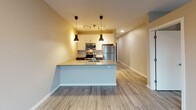 Located at 2323 NE Jackson St in Minneapolis, MN, this modern single-floor unit offers a thoughtfully designed open-concept layout that seamlessly connects the kitchen and living areas. The kitchen is a standout feature, equipped with stainless steel appliances including a refrigerator, electric range, and microwave. A central island with a double stainless steel sink and quartz-style countertops provides both workspace and casual dining potential. Dark cabinetry on the lower level contrasts with white upper cabinets, creating a contemporary two-tone aesthetic. Pendant lighting and a track light system illuminate the space with a warm, inviting glow. Light wood-style vinyl plank flooring runs throughout the unit, lending a clean and cohesive feel. The living area benefits from a large window fitted with a roller shade, allowing natural light to fill the room while offering views of the surrounding Minneapolis neighborhood. The bathroom is efficiently designed with tile-style flooring, a dark vanity with drawer storage, a wall-mounted grab bar, and clean white walls that maintain the unit's modern sensibility. The overall design is characterized by neutral tones, contemporary fixtures, and practical finishes that make for a comfortable and functional living environment.