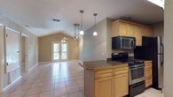 This single-story residence at Stadium Place offers a well-organized layout with consistent light tile flooring running throughout. The open-concept kitchen and living area serves as the heart of the home, where a vaulted ceiling adds a sense of vertical space and airiness. The kitchen is equipped with dark granite countertops, light wood cabinetry, black appliances including a range and refrigerator, a built-in microwave, and pendant lighting that illuminates the peninsula workspace. The living area extends toward a set of glass French doors that invite natural light and provide outdoor access, complemented by a ceiling fan overhead.

Multiple bedrooms are present, each featuring ceiling fans and windows that bring in natural light with views of surrounding greenery. The bedrooms connect to a spacious walk-in closet outfitted with wire shelving systems for organized storage. The bathrooms include a full bath with a soaking tub and shower combination, a second full bath with a vanity and mirror, and a compact half bath—all finished with light wood cabinetry and neutral-toned walls that lend a clean, cohesive aesthetic throughout the home.