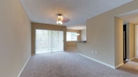 This single-floor residence offers a bright and welcoming interior defined by an open-concept layout that seamlessly connects the living and dining areas. The living room is finished with soft, plush wall-to-wall carpeting and features a ceiling fan with a light fixture, providing both comfort and functionality. A full-length sliding glass door dressed with vertical blinds allows an abundance of natural light to flow into the space while offering direct access to the outdoors and views of surrounding greenery.

Adjacent to the living area, the dining space is illuminated by a hanging pendant light, creating a warm and intimate atmosphere. A pass-through counter connects the dining area to the kitchen, enhancing the open feel of the floor plan and making the space ideal for entertaining. The kitchen features dark countertops visible through the pass-through opening, offering a subtle contrast to the neutral warm-toned walls that run throughout the residence.

Textured ceilings add a classic architectural detail, while clean white baseboards frame each room with a crisp finish. The consistent warm beige wall tones lend a cohesive and inviting ambiance throughout, making this single-floor space feel comfortable, airy, and well-appointed.