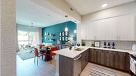 This single-floor residence showcases a thoughtfully designed open-concept layout that seamlessly connects the kitchen, dining, and living areas. The kitchen is outfitted with two-tone cabinetry — crisp white upper cabinets paired with dark wood lower cabinets — complemented by light quartz countertops, a subway tile backsplash, and a full suite of stainless steel appliances including a French door refrigerator, range, and over-the-range microwave. A peninsula with pendant lighting provides additional workspace and visual separation between the kitchen and dining area.

The living room is defined by a striking teal accent wall adorned with floating shelves, creating a bold yet cohesive focal point. Light wood-style flooring runs throughout the main living areas, while a ceiling fan and sliding glass doors allow natural light and outdoor views to enhance the space. The bedroom continues the teal color palette, featuring ample natural light through slatted blinds, a seating nook, and plush carpeting. The bathroom offers a dark wood vanity with a white countertop, a tub-shower combination with subway tile surround, and wood-look tile flooring, delivering a clean and functional finish throughout.