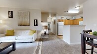 This single-story residence offers a thoughtfully designed open-concept floor plan that seamlessly connects the main living areas. The living room is a welcoming space finished with plush wall-to-wall carpeting, neutral-toned walls, and large windows that allow natural light to filter in. A ceiling fan and decorative drapery add functional and aesthetic detail to the room.

The kitchen is well-equipped, featuring warm oak cabinetry extending to the ceiling for generous storage, white appliances including a refrigerator, range, microwave, and dishwasher, and light hardwood flooring. A peninsula counter connects the kitchen to the adjacent dining area, which comfortably accommodates a full dining set and includes a closet for additional storage.

The bedrooms are carpeted and spacious, each offering room for substantial furniture. One bedroom benefits from a large window with outdoor views, while another is served by a walk-in closet with full-length hanging storage. The bathroom features a wood-vanity with an integrated sink, tile flooring, and a large mirror. Neutral finishes and a consistent color palette throughout the residence create a cohesive and calm overall ambiance.