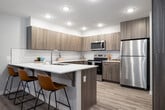This well-designed 2-bedroom, 2-bathroom residence offers a thoughtfully organized single-level layout that maximizes every square foot. The open-concept kitchen and living area serves as the heart of the home, featuring a U-shaped kitchen outfitted with two-tone wood-grain cabinetry, white quartz countertops, a classic subway tile backsplash, and a full suite of stainless steel appliances including a refrigerator, electric range, and built-in microwave. A peninsula with bar seating provides additional prep space and casual dining options, flowing seamlessly into the adjoining living room. The living area is bright and welcoming, with a door that allows natural light to filter in. Light wood-tone luxury vinyl plank flooring runs throughout the main living spaces, adding warmth and continuity. Both bedrooms are carpeted for comfort and feature windows with blinds, providing a calm and restful atmosphere. The primary bedroom offers a comfortable footprint suitable for a queen or king bed setup. Each of the two bathrooms is finished with wood-grain vanities, white quartz countertops, large mirrors, and wood-look flooring. One bathroom includes a shower/tub combo, while the other features a walk-in shower. A hallway connects the bedrooms and bathrooms, keeping the layout private and functional.