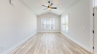 Located in Leland, NC, this single-story home offers a thoughtfully designed layout across two bedrooms and three bathrooms. The kitchen is a standout feature, showcasing gray shaker-style cabinetry, granite countertops, a large center island with a matte black faucet, subway tile backsplash, stainless steel appliances including double wall ovens and a French door refrigerator, and warm hardwood-style flooring throughout. Pendant lighting above the island adds a refined touch. The living and dining areas feature the same light hardwood floors, tray ceilings with beadboard detailing, and an elegant multi-arm chandelier, with windows offering views of the well-maintained neighborhood streetscape. The spacious primary bedroom is finished with plush carpet, elevated ceilings, a ceiling fan, and a double-door closet with Craftsman-style hardware. The secondary bedroom mirrors this comfort with carpet flooring, a ceiling fan, and a large window that fills the room with natural light. The bathrooms are clean and modern, featuring gray cabinetry with black hardware and wood-look tile flooring. The attached garage provides generous storage space with a window and automatic opener. Outside, a concrete driveway leads to a neatly landscaped front yard within a charming residential community.