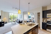 Located at 70 Upper Rock Circle in Rockville, MD, this well-appointed 2-bedroom, 4-bathroom residence offers a thoughtfully designed single-level layout with modern finishes throughout. The open-concept kitchen and living area serves as the heart of the home, anchored by a spacious center island with quartz countertops, a stainless steel sink, and stylish pendant lighting. Dark cabinetry, a mosaic tile backsplash, stainless steel appliances, and hardwood-style flooring complete the kitchen, which also features convenient in-unit stacked washer and dryer access. The living room is bright and inviting, highlighted by a large floor-to-ceiling window that frames lush, verdant outdoor views, with soft carpet underfoot adding warmth and comfort. Both bedrooms are well-proportioned and serene, each with natural light filtering through windows overlooking greenery. The primary bedroom includes a ceiling fan and an en-suite bath with a generous vanity, dark navy cabinetry, and a walk-in closet with built-in shelving. Additional bathrooms mirror the same refined aesthetic, featuring large mirrors, neutral tile, and clean, contemporary fixtures. Two dedicated closets provide ample storage throughout the residence, rounding out a functional and elegant living experience.