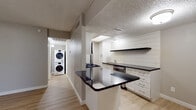 This single-floor residence offers a thoughtfully designed layout with contemporary finishes throughout. Light-toned hardwood-style flooring flows seamlessly across all living areas, creating a cohesive and inviting atmosphere.

The kitchen is a standout feature, showcasing white shaker-style cabinetry paired with striking dark countertops and a peninsula that provides additional seating and prep space. A shiplap accent wall adds a modern farmhouse touch, complemented by open floating shelves. Stainless steel appliances, including a gas range, refrigerator, and dishwasher, complete the functional cooking space. A skylight panel overhead adds a welcome touch of natural light.

The living area is open and bright, with a ceiling fan and sliding glass doors that lead to a private patio, offering a seamless connection to the outdoors. The bedroom is spacious and airy, featuring neutral walls and generous proportions. An expansive walk-in closet provides ample storage with built-in shelving and hanging rods.

The bathroom is elegantly appointed with large-format marble-look tile surrounding the soaking tub and shower. A stacked washer and dryer unit is conveniently located in a dedicated in-unit laundry nook. Textured ceilings are found throughout, adding a classic residential character to the space.