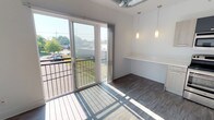 This thoughtfully designed studio offers a single-floor open layout that maximizes functionality within a compact footprint. The kitchen is a standout feature, outfitted with stainless steel appliances including an electric range, over-the-range microwave, dishwasher, and refrigerator. Light wood-toned cabinetry extends to the ceiling, paired with crisp white quartz countertops and an undermount sink, creating a clean, modern aesthetic. Wood-look luxury vinyl flooring runs throughout, tying the space together seamlessly. The main living area is bathed in natural light from a large sliding glass door that opens to a private balcony, offering open outdoor views. Pendant lighting adds a stylish touch above the built-in counter that serves as a dining or workspace ledge. An exposed duct detail adds an industrial accent to the otherwise minimalist design. The full bathroom features a wide vanity with white quartz countertop, a wood-toned cabinet base, a large mirror, and a glass-enclosed shower. A dedicated in-unit laundry closet accommodates a stacked washer and dryer with additional wire shelving for storage. Overall, the space presents a bright, efficient, and contemporary living environment with practical amenities throughout.