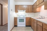 Located at 510 E 21st St in Marshfield, Wisconsin, this single-floor, 2-bedroom, 1-bathroom unit offers a practical and efficiently organized layout. The kitchen is well-appointed with warm wood cabinetry extending to the upper walls, offering ample storage, and includes a white electric range, refrigerator, and a stainless sink set along an L-shaped counter with light-colored tile flooring. A hallway entry features a built-in open shelving unit with multiple tiers, ideal for additional storage. The living room provides a comfortable gathering space connected to the main hallway. Both bedrooms are carpeted and feature sliding-door closets with rod and shelf storage. The primary bedroom is generously sized and benefits from a window with outdoor views and a baseboard heating unit. The second bedroom also includes a window with natural light and neighborhood views. The full bathroom is cleanly finished with a single-sink vanity, medicine cabinet mirror, and tile flooring. A dedicated laundry area and a utility closet housing a water heater round out the unit's practical amenities. Two hallways efficiently connect all rooms throughout the space.