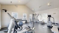 Located at 77 Barclay Place Ct in Charlottesville, Virginia, this dedicated fitness center offers a well-equipped workout space designed to support a range of exercise routines. The room features striking vaulted ceilings that create an open, airy atmosphere despite the compact footprint, with track lighting overhead providing focused illumination throughout the space.

Natural light flows in generously through multiple windows fitted with horizontal blinds, offering views of the surrounding outdoor area, including a glimpse of a pool. Full-length mirrors along one wall visually expand the space and allow users to monitor their form during workouts.

The fitness center is outfitted with a comprehensive selection of equipment, including treadmills, a stationary bike, a stair climber, a multi-station cable and weight machine, a rowing machine, a flat bench, and a dumbbell rack. A wall-mounted flat-screen television adds a convenient entertainment option for cardio sessions.

The flooring is durable and dark-toned, suited for high-traffic fitness use, while the crisp white walls maintain a clean, professional aesthetic. The overall ambiance is bright, functional, and well-organized, making this fitness center a practical and accessible amenity for residents of the Barclay Place community.