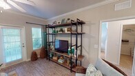 This single-floor residence offers a thoughtfully designed layout that balances comfort and functionality. The living room serves as the heart of the home, featuring warm hardwood-style flooring, crown molding, a ceiling fan, and soft sage-green accent walls that create a calming coastal ambiance. An open-concept design connects the living area to the kitchen via a breakfast bar with bar seating, making it ideal for entertaining. The galley-style kitchen is well-equipped with warm wood cabinetry, tile backsplash, black appliances including a range and built-in microwave, a double stainless steel sink, and tile flooring. Adjacent to the living area, a dedicated dining nook accommodates a round table beneath a multi-light chandelier. The primary bedroom features plush carpeting, crown molding, a ceiling fan, and a window with natural light. The second bedroom offers a similarly restful atmosphere with soft blue accent walls and coordinating carpet. Both bathrooms are outfitted with tub-shower combinations, white vanities, and crown molding details. Throughout the residence, consistent trim work and a cohesive coastal color scheme in teal, taupe, and white tie the space together into a harmonious whole.