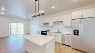 Located at 6155 24th St S in Fargo, North Dakota, this thoughtfully designed one-bedroom, one-bathroom unit offers a clean, modern aesthetic with a bright and efficient layout. The open-concept kitchen and living area serves as the heart of the home, featuring crisp white shaker cabinetry, a central island with a light countertop, and a full suite of stainless steel appliances including a side-by-side refrigerator with ice and water dispenser, a dishwasher, and a slide-in range. A stylish industrial-style pendant light anchors the kitchen, while light wood-style luxury vinyl flooring flows throughout the main living areas, adding warmth and continuity. The living room is filled with natural light from a sliding glass door that opens to an outdoor view, creating an airy, open feel. The bedroom is comfortably sized with soft carpeting, a large window overlooking a green landscape, and a double-door closet offering ample storage. The bathroom is clean and functional, featuring a tub-shower combo with matte black fixtures and wood-style flooring. A dedicated in-unit laundry space with a full-size Whirlpool washer and dryer and overhead shelving adds exceptional everyday convenience. The unit's crisp white walls, modern finishes, and abundant natural light create a fresh, inviting atmosphere throughout.