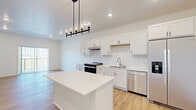 Located at 6155 24th St S in Fargo, North Dakota, this thoughtfully designed one-bedroom, one-bathroom unit offers a clean, modern aesthetic with a bright and efficient layout. The open-concept kitchen and living area serves as the heart of the home, featuring crisp white shaker cabinetry, a central island with a light countertop, and a full suite of stainless steel appliances including a side-by-side refrigerator with ice and water dispenser, a dishwasher, and a slide-in range. A stylish industrial-style pendant light anchors the kitchen, while light wood-style luxury vinyl flooring flows throughout the main living areas, adding warmth and continuity. The living room is filled with natural light from a sliding glass door that opens to an outdoor view, creating an airy, open feel. The bedroom is comfortably sized with soft carpeting, a large window overlooking a green landscape, and a double-door closet offering ample storage. The bathroom is clean and functional, featuring a tub-shower combo with matte black fixtures and wood-style flooring. A dedicated in-unit laundry space with a full-size Whirlpool washer and dryer and overhead shelving adds exceptional everyday convenience. The unit's crisp white walls, modern finishes, and abundant natural light create a fresh, inviting atmosphere throughout.