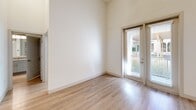 Located at 2600 Lakefront Trail in Rockwall, TX, this one-bedroom, one-bathroom residence offers a thoughtfully designed open-concept layout with impressively soaring ceilings that amplify the sense of space throughout. Light-toned hardwood-style flooring flows seamlessly through the combined living, dining, and kitchen area, enhancing the bright, airy ambiance created by large windows and recessed lighting. The kitchen is a standout feature, boasting a substantial granite-topped island with an undermount sink, soft gray shaker cabinetry, a geometric tile backsplash, stainless steel appliances including a refrigerator, range, and microwave, and a dedicated wine rack and pantry for added convenience. Sliding glass doors lead from the living area to a private balcony, inviting natural light and outdoor access. The spacious bedroom features plush carpet flooring, tall ceilings, and natural light from a window with outdoor views. Three closets, including a generously sized walk-in with wire shelving systems, provide ample storage. The bathroom is well-appointed with granite countertops, gray cabinetry, a large vanity mirror, and a subway-tiled soaking tub and shower combination, with direct access to the walk-in closet.