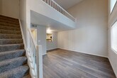 Located at 1281 Brockett Rd in Clarkston, GA, this two-story residence offers a well-organized layout across two floors. The main level opens into a bright entrance that flows into a combined living and dining area, highlighted by dramatic double-height ceilings, large windows that invite abundant natural light, and durable hardwood-style flooring throughout. A carpeted staircase with white-railed banisters leads to the upper level, which overlooks the living space below through an open balcony railing. The kitchen is well-appointed with white shaker-style cabinetry, granite-look countertops, black appliances including a refrigerator, gas range, and dishwasher, along with a convenient pass-through window to the living area. Additional main-level features include a utility room, laundry area, and ample closet space. The generously sized primary bedroom on the upper floor features hardwood-style flooring, a large window with exterior views, and vaulted ceilings that enhance the sense of space. Two full bathrooms serve the home — one featuring a tub/shower combo, and the primary bath offering a granite-topped vanity with built-in shelving. The overall aesthetic is clean and contemporary, with neutral tones and updated finishes throughout.