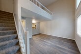 Located at 1281 Brockett Rd in Clarkston, GA, this two-story residence offers a well-organized layout across two floors. The main level opens into a bright entrance that flows into a combined living and dining area, highlighted by dramatic double-height ceilings, large windows that invite abundant natural light, and durable hardwood-style flooring throughout. A carpeted staircase with white-railed banisters leads to the upper level, which overlooks the living space below through an open balcony railing. The kitchen is well-appointed with white shaker-style cabinetry, granite-look countertops, black appliances including a refrigerator, gas range, and dishwasher, along with a convenient pass-through window to the living area. Additional main-level features include a utility room, laundry area, and ample closet space. The generously sized primary bedroom on the upper floor features hardwood-style flooring, a large window with exterior views, and vaulted ceilings that enhance the sense of space. Two full bathrooms serve the home — one featuring a tub/shower combo, and the primary bath offering a granite-topped vanity with built-in shelving. The overall aesthetic is clean and contemporary, with neutral tones and updated finishes throughout.