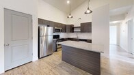 Located in Farmington, Utah, this well-appointed single-floor residence offers three bedrooms, two full bathrooms, and a thoughtfully designed layout. The living area makes an immediate impression with its soaring vaulted ceilings, neutral carpet flooring, and a door leading directly to a private balcony, filling the space with natural light and a sense of openness. Wood-look flooring transitions from the living area into the kitchen, which is a standout feature of the home. Dark espresso cabinetry pairs elegantly with granite countertops, a classic subway tile backsplash, and a full suite of stainless steel appliances, including a refrigerator, range, microwave, and dishwasher. The bedrooms are carpeted and bright, with multiple windows offering outdoor views of the surrounding Farmington landscape. Three closets provide ample storage throughout, including dedicated hanging rods and shelving. Both bathrooms feature tile flooring, dark wood vanities with granite counters, and tub-shower combinations. A utility room with built-in shelving and an electrical panel, along with a dedicated laundry area, add to the home's functional appeal. Clean lines, neutral tones, and modern finishes create a cohesive and inviting atmosphere throughout.