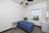This 120 square foot studio apartment, located in the heart of San Diego, offers a compact yet functional living space. The room is characterized by its bright and airy atmosphere, courtesy of a large multi-pane window that floods the space with natural light and provides pleasant city views. The hardwood flooring adds warmth and durability to the space.

The studio's layout is efficiently designed to maximize the available area. A comfortable full-size bed with a blue cover serves as the centerpiece, suitable for both sleeping and lounging. White walls and trim create a clean, spacious feel, while dark baseboards add a subtle contrast.

A small white side table and a light blue plant stand with a potted plant add touches of practicality and nature to the room. The space also includes a compact white vanity unit with a mirror, suggesting an integrated bathroom area.

The high ceilings, adorned with simple light fixtures, enhance the sense of spaciousness. Despite its small footprint, the room appears uncluttered and well-organized, making it an ideal choice for those seeking a minimalist urban lifestyle in downtown San Diego.