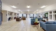 Located at 12949 Eastbrook Dr Club in El Paso, TX, this single-story community clubhouse offers a generously sized, well-appointed gathering space designed to serve a variety of resident needs. The main area is expansive and open, featuring large light-colored ceramic tile flooring that runs throughout the entire facility, contributing to a bright and cohesive feel. Elevated ceilings with flush fluorescent lighting further enhance the sense of spaciousness and keep the interior well-lit at all times.

The primary lounge area is thoughtfully arranged with multiple seating groups, including sofas, armchairs, and accent tables, accommodating both casual socializing and larger group gatherings. A dining table with chairs provides a dedicated space for shared meals or meetings. A striking dark stacked-stone accent wall serves as a bold architectural focal point, adding texture and visual contrast to the otherwise neutral interior palette.

Adjacent to the main lounge is a game room featuring a full-size pool table, comfortable seating, and a wall-mounted television, making it an inviting space for recreation. A separate study and business nook includes built-in shelving, individual desk workstations, and seating, ideal for remote work or quiet focus. Large windows throughout allow abundant natural light to fill each area while offering views of the surrounding neighborhood.