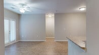 This single-story unit is designed with a practical, open-concept layout that connects the kitchen and living areas seamlessly. The kitchen is equipped with dark espresso cabinetry, granite-style laminate countertops, black appliances including a range, microwave, and refrigerator, and a peninsula with a built-in sink that opens toward the main living space. A dedicated laundry area is conveniently located just off the kitchen, housing a full-size washer and dryer.

The living area is generously sized, featuring a ceiling fan, neutral warm-gray walls, and French doors that provide natural light and outdoor access. Wood-look plank flooring runs throughout the main living spaces and bedrooms, offering a cohesive and easy-to-maintain finish.

The bedrooms are well-proportioned, each with ceiling fans and natural light from windows with blinds. The primary bedroom includes access to a walk-in closet with built-in shelving. Two bathrooms serve the unit — one features a dark-vanity with a large mirror and walk-in shower, while the second includes a full tub/shower combo, matching dark cabinetry, and tile flooring. The overall aesthetic is clean, modern, and move-in ready.