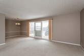 This single-floor residence offers a thoughtfully laid-out floor plan designed for comfortable everyday living. The expansive living room is a standout feature, highlighted by a textured ceiling, plush wall-to-wall carpeting in a warm neutral tone, and large sliding glass doors that open to a private balcony overlooking a natural, tree-lined setting. Natural light fills the space throughout the day, creating a bright and welcoming ambiance. An adjoining dining area is enhanced by a classic chandelier, adding an elegant touch to the open flow between living and entertaining spaces. The kitchen is outfitted with white raised-panel cabinetry, ample counter space, a double stainless steel sink, a dishwasher, and a pass-through window that connects to the main living area, maintaining an open feel. The bedrooms are generously sized, each featuring soft carpeting, neutral-toned walls, ceiling fans with integrated lighting, and windows that bring in views of the surrounding greenery. The bathrooms include tile flooring in a classic diamond pattern, a tub-shower combination with tiled surround, white vanity cabinetry, and mirrored storage. Overall, the space presents a clean, neutral palette throughout, offering a versatile and move-in-ready environment.