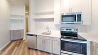 Located at 401 A St in Wilmington, DE, this modern 2-bedroom, 1-bathroom unit offers a thoughtfully designed, single-floor layout with clean, contemporary finishes throughout. A central hallway connects the key living spaces, with light wood-look flooring running through the main areas and plush carpet in the bedrooms.

The kitchen is efficiently outfitted with stainless steel appliances, including a range, over-the-range microwave, dishwasher, and full-size refrigerator. Light wood cabinetry at the base pairs with crisp white upper cabinets and open shelving, all set against white countertops for a bright, modern aesthetic.

The primary bedroom offers a comfortable footprint with soft carpeting and access to a dedicated laundry closet housing a stacked washer and dryer — a convenient in-unit feature. The second bedroom is bright and airy, benefiting from a window with city views over the Wilmington skyline.

The bathroom presents a clean, minimalist design with large-format tile flooring, a wood-toned vanity with a white countertop, dual mirrored medicine cabinets, and matte black fixtures that add a contemporary touch. The hallway also features an accessible electrical panel. Overall, the unit delivers a modern, functional living environment with quality finishes throughout.