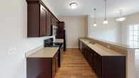 This two-floor home offers a thoughtfully designed layout across its main and lower levels. The main floor centers around an open-concept living area with plush carpeting, neutral warm-toned walls, and generous natural light streaming through multiple windows. A pendant-lit dining area connects seamlessly to the galley-style kitchen, which is outfitted with rich dark cabinetry, granite-style countertops, stainless steel appliances, and hardwood-style flooring — a practical yet stylish space for everyday living. A breakfast bar provides an additional surface that bridges the kitchen and living areas. Bedrooms on this level are carpeted and bright, with ample closet space including walk-in options. A full bathroom features a double-sink vanity with dark wood cabinetry, stone-look countertops, and tile flooring, offering a refined and functional design. The lower level expands the home's versatility with a large, open carpeted recreation area featuring a drop tile ceiling, recessed lighting, and sliding glass doors that open to a lush outdoor greenspace. Additional windows on this level bring in natural light, making it feel welcoming. A staircase connects both floors with ease. Throughout, the home maintains a consistent, clean aesthetic with neutral tones and quality finishes.