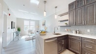 Located at 50 Main St in Hackensack, NJ, this single-floor residence offers a thoughtfully designed open-concept layout filled with natural light. Light hardwood flooring flows throughout the main living areas, creating a clean and cohesive aesthetic.

The kitchen is a standout feature, showcasing rich dark espresso cabinetry that extends to the ceiling for ample storage, complemented by sleek white quartz countertops and a herringbone-patterned tile backsplash. A peninsula with bar seating serves as both a functional workspace and a casual dining area, illuminated by modern pendant lighting. Stainless steel appliances, including a gas range, built-in microwave, dishwasher, and refrigerator, complete the well-equipped space. Open floating shelves add a contemporary touch.

The living area is bright and welcoming, with large windows that invite natural light and provide views of the surrounding neighborhood. Neutral wall tones and a clean, modern design create a relaxed and versatile atmosphere.

The bedroom is a comfortable retreat, featuring a ceiling fan, a window with natural light, and carpeted flooring for added warmth. The bathroom is finished with dark wood cabinetry, a marble-topped vanity, light wood-look tile flooring, and a tall linen tower for storage, reflecting the same refined design language found throughout the residence.