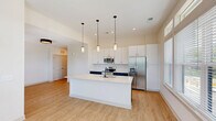 Located at 1821 Chatham Flats Drive in Apex, NC, this thoughtfully designed 2-bedroom, 2-bathroom residence offers a comfortable and modern single-floor layout. The open-concept living, dining, and kitchen area serves as the heart of the home, with light wood-look flooring flowing throughout. The kitchen is a standout feature, boasting white upper cabinetry, navy lower cabinets, quartz countertops, a large center island with pendant lighting overhead, and a full suite of stainless steel appliances including a range, microwave, and french door refrigerator. Natural light pours in through large windows, enhancing the bright, airy atmosphere. The primary bedroom is generously sized with plush carpet, a ceiling fan, and a walk-in closet. The en-suite primary bathroom features a dual-sink vanity with dark cabinetry, quartz countertops, and a glass-enclosed walk-in shower. The second bedroom is equally well-appointed with carpet flooring and ample natural light. A second full bathroom includes a tub-shower combo and single vanity. Additional highlights include a dedicated laundry area, a built-in hallway entry nook with shelving and hooks, three closets, and a private balcony.