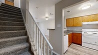 This two-story home in Killeen, TX offers a well-organized layout spread across two floors. The main level features a combined kitchen and living area with durable wood-look tile flooring throughout. The kitchen is equipped with warm oak cabinetry, granite-style countertops, a built-in dishwasher, and a peninsula pass-through that connects seamlessly to the living space. The living room is bright and open, featuring a ceiling fan with light fixture and a sliding glass door with vertical blinds that allows natural light to fill the room.

A carpeted staircase with a white-railed banister leads to the upper level, where both bedrooms are located. The primary bedroom offers generous proportions with plush carpeting and a double-door closet. The second bedroom also features soft carpeting and neutral tones. Both bathrooms are outfitted with oak vanities, white countertops, large mirrors, and wood-look tile flooring. The full bathroom includes a tub-shower combination, while the additional bathroom provides a vanity and toilet.

Throughout the home, neutral gray and beige tones create a clean, cohesive aesthetic. The consistent use of wood-look flooring on the main level and carpet in the bedrooms adds both practicality and comfort to this functional two-story layout.