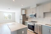 Located at 2119 Post Rd in Warwick, Rhode Island, this thoughtfully designed one-bedroom, one-bathroom unit offers a efficient and modern living experience on a single floor. The open-concept layout seamlessly connects the kitchen and combined dining and living area, creating a bright, cohesive space bathed in natural light from well-placed windows.

The kitchen is a standout feature, showcasing two-tone cabinetry with sleek gray lower cabinets and light upper cabinets, white subway tile backsplash, crisp white countertops, and a full suite of stainless steel appliances including a refrigerator, range, microwave, and dishwasher. A central island provides additional prep space and a natural gathering point.

Light wood-look flooring runs throughout the main living areas, while the bedroom features plush carpeting and a generously sized window that frames outdoor greenery and allows ample natural light. Two closets, including one with built-in wire shelving, offer practical storage solutions.

The bathroom is clean and contemporary, featuring a tiled tub-shower combo, a gray vanity with white countertop, and a large mirror. Additional utility and laundry rooms round out the functional layout of this well-appointed Warwick residence.
