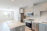 Located at 2119 Post Rd in Warwick, Rhode Island, this thoughtfully designed one-bedroom, one-bathroom unit offers a efficient and modern living experience on a single floor. The open-concept layout seamlessly connects the kitchen and combined dining and living area, creating a bright, cohesive space bathed in natural light from well-placed windows.

The kitchen is a standout feature, showcasing two-tone cabinetry with sleek gray lower cabinets and light upper cabinets, white subway tile backsplash, crisp white countertops, and a full suite of stainless steel appliances including a refrigerator, range, microwave, and dishwasher. A central island provides additional prep space and a natural gathering point.

Light wood-look flooring runs throughout the main living areas, while the bedroom features plush carpeting and a generously sized window that frames outdoor greenery and allows ample natural light. Two closets, including one with built-in wire shelving, offer practical storage solutions.

The bathroom is clean and contemporary, featuring a tiled tub-shower combo, a gray vanity with white countertop, and a large mirror. Additional utility and laundry rooms round out the functional layout of this well-appointed Warwick residence.