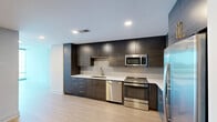 Located in the heart of downtown Raleigh, this high-rise unit on the 14th floor offers a thoughtfully designed one-bedroom, one-bathroom layout with a clean, modern aesthetic. Light wood-tone flooring flows seamlessly throughout the space, complementing the neutral palette of white and soft gray walls.

The open kitchen is a standout feature, outfitted with two-tone cabinetry — rich dark wood uppers paired with deep teal-toned lowers — white quartz countertops, a subway tile backsplash, and a full suite of stainless steel appliances including a gas range, built-in microwave, dishwasher, and French door refrigerator with ice dispenser.

The living area benefits from expansive floor-to-ceiling windows that frame striking panoramic views of the Raleigh skyline, flooding the space with abundant natural light. The bedroom continues this design language with its own floor-to-ceiling window wall offering city views, a dedicated closet, and access to the full bathroom.

The bathroom features large-format tile flooring, a soaking tub with shower, a wide single-sink vanity with contemporary cabinetry, and recessed lighting. A dedicated closet completes the unit's functional layout. The overall ambiance is sleek, bright, and urban — ideal for those seeking a modern downtown lifestyle.