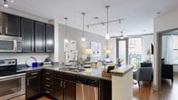 Located at 201 Park at North Hills St in Raleigh, NC, this single-floor residence offers a well-designed open-concept layout with modern finishes and comfortable living spaces. The kitchen is a standout feature, equipped with dark espresso cabinetry, granite countertops, stainless steel appliances, a subway tile backsplash, and a central island with pendant lighting overhead. Track lighting and a double sink add both functionality and style to this well-appointed space. The open layout flows seamlessly into the living area, where hardwood floors, a ceiling fan, and a glass-panel door lead out to a private balcony with outdoor views. The bedroom is a serene retreat, featuring hardwood floors, large windows that welcome natural light, and a ceiling fan. The bathroom is cleanly finished with granite countertops, dark cabinetry, and a shower-tub combination. A stacked in-unit washer and dryer provide added convenience. The entryway is practical and welcoming, complete with a coat hook wall rack and easy access to all areas of the home. Neutral gray tones and warm wood flooring tie the entire space together, creating a cohesive and inviting ambiance throughout.