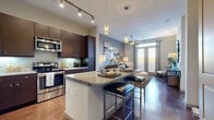 Located in the Galleria area of Houston, Texas, this single-floor residence offers a thoughtfully designed open-concept layout with contemporary finishes and a warm, modern aesthetic. The kitchen serves as a central hub of the home, showcasing rich dark-wood cabinetry, granite countertops, a large center island with bar seating, stainless steel appliances, and elegant pendant lighting — all set above wood-look flooring that extends seamlessly into the living and dining areas. The living room is bathed in natural light from expansive floor-to-ceiling windows and sliding glass doors, complemented by a ceiling fan and tasteful décor. A versatile transitional space connects the main living area to the private quarters, featuring additional natural light and access to a well-lit bathroom. The bedrooms offer plush carpeted floors, generous windows with garden views, and ceiling fans, creating a calm and restful atmosphere. The bathroom is finished with granite countertops, dark wood cabinetry, tile flooring, and a walk-in closet with built-in shelving. A concealed in-unit laundry area adds everyday convenience. The overall ambiance throughout the residence is contemporary and refined, with a cohesive neutral palette and high-quality finishes at every turn.