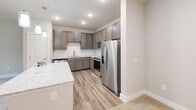 Located at 7011 Lucia Road in Charlotte, NC, this 1-bedroom, 2-bathroom residence offers a thoughtfully designed single-floor layout with contemporary finishes throughout. The kitchen is a standout feature, showcasing warm taupe shaker-style cabinetry, light granite countertops, a classic white subway tile backsplash, and a full suite of stainless steel appliances including a refrigerator, range, dishwasher, and built-in microwave. A kitchen island provides additional prep and counter space, while wood-look vinyl flooring ties the area together with a clean, modern aesthetic. The spacious bedroom features soft carpeting, a ceiling fan with light, and a large window that invites natural light and offers pleasant outdoor views. The two bathrooms are finished with matching granite vanity tops and wood-toned cabinetry, maintaining a cohesive design. One bathroom includes a sleek walk-in shower with a sliding glass door and brushed nickel hardware, while the other is equipped with an accessibility grab bar for added convenience. A dedicated in-unit laundry room houses a full-size washer and dryer with overhead wire shelving for storage. Hallways connect the spaces efficiently, and a closet provides additional storage. The overall ambiance is clean, modern, and move-in ready.