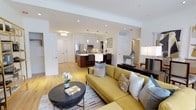 This single-floor residence offers 2 bedrooms and 2.5 bathrooms arranged in an open, flowing layout that maximizes the sense of space. The living area serves as the heart of the home, featuring light hardwood flooring, crown molding, and recessed lighting that create a clean, polished aesthetic. The space is anchored by a welcoming seating arrangement and opens seamlessly into the kitchen and dining areas.

The kitchen is thoughtfully designed with white upper cabinetry, rich dark wood lower cabinets, stainless steel appliances including a refrigerator and microwave, and a central island with bar seating and pendant lighting above. The contrasting cabinetry tones add visual depth while maintaining a modern, cohesive look.

The open-concept design allows natural sightlines across all main living areas, enhancing the spacious feel of the interior. Crisp white walls, consistent hardwood flooring throughout, and carefully placed lighting contribute to a bright and airy ambiance. The overall design balances contemporary style with functional living, making it a practical and visually appealing residence.