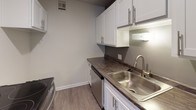 Located at 30 College Ave SE in Grand Rapids, Michigan, this single-floor unit offers a well-organized layout designed for comfortable everyday living. The living area features light-toned luxury vinyl plank flooring, neutral walls, and ample natural light streaming through windows with horizontal blinds. A seamless opening connects the living space to the kitchen, which is equipped with white cabinetry featuring modern hardware, dark laminate countertops, a stainless steel sink and faucet, and stainless steel appliances including a refrigerator, range, and dishwasher. Adjacent to the living area is a versatile secondary space with matching vinyl plank flooring, a louvered closet, and a window that brings in natural light. The bedrooms are carpeted in a neutral gray tone and include windows with blinds for privacy and natural light; one bedroom features a wall-mounted HVAC unit and multiple windows. A dedicated vanity area connects the bedroom wing to the bathroom, offering a marble-style countertop, white cabinetry, and a large wall mirror. The full bathroom includes white tile wainscoting, a tub-shower combination, a single-basin vanity with dark countertop, and classic mosaic tile flooring. Throughout the unit, a consistent neutral color palette and clean finishes create a cohesive and functional living environment.