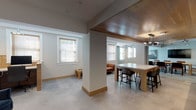 This thoughtfully designed single-floor office space blends contemporary aesthetics with functional workspaces, creating a professional yet inviting environment. Polished concrete flooring runs throughout, providing a clean, cohesive foundation that ties each area together seamlessly.

The centerpiece of the space is a glass-walled conference room, offering full visibility while maintaining acoustic privacy. Inside, a solid natural wood conference table is surrounded by leather chairs, complemented by industrial-style pendant lighting, a wall-mounted display screen, and bold artwork that adds character to the room.

An open collaboration zone features a high-top table with bar-height seating, ideal for informal meetings or shared work sessions. Structural columns subtly define zones without disrupting the open flow, while multiple windows fitted with wood-slat blinds invite abundant natural light throughout.

A dedicated workstation area provides semi-private desking separated by warm wood-paneled dividers, accompanied by plush navy accent chairs that offer a comfortable lounge setting alongside the desks.

The kitchenette is a standout feature, finished with light wood cabinetry, a marble-toned countertop, a stainless steel sink, and an under-counter refrigerator. A decorative star-patterned tile backsplash adds a striking visual element, while a wall-mounted TV and wood-paneled ceiling overhead complete the refined aesthetic of this well-appointed office.